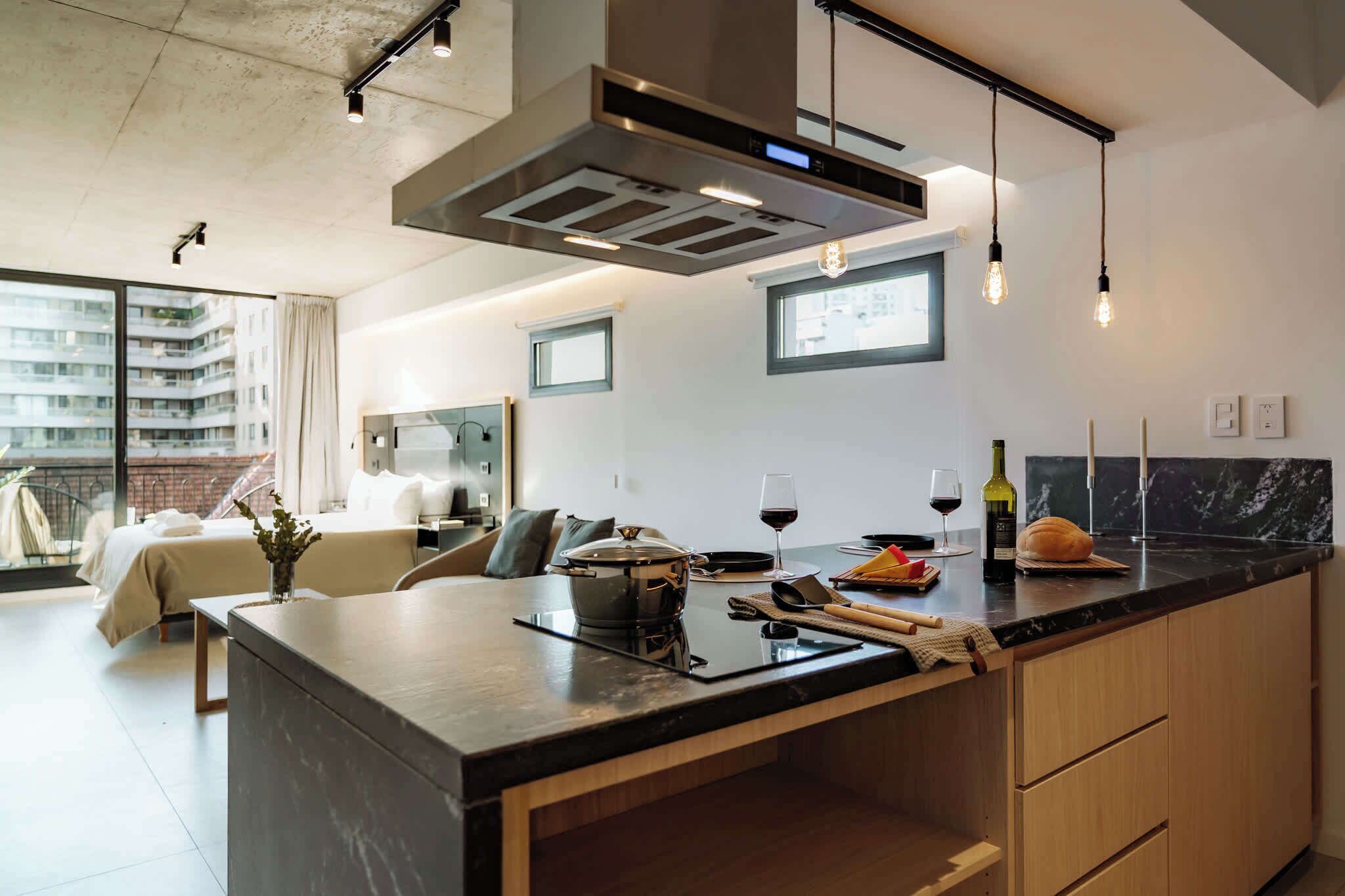 A modern kitchen with a central island, built-in appliances, pendant lighting, and a view of the city.