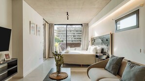 Ett modernt hotellrum med en säng, en soffa, en TV och utsikt över en byggnad utanför.
