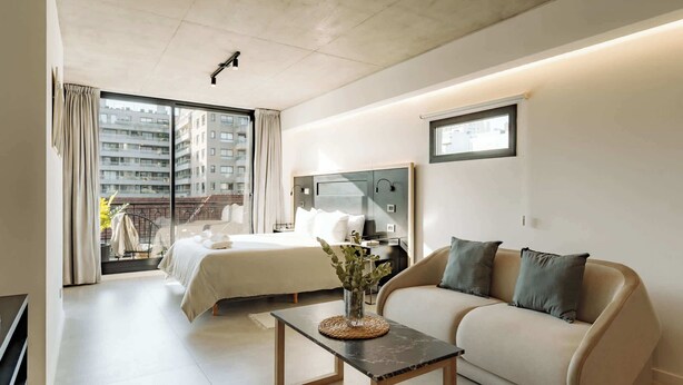 Ett modernt hotellrum med en säng, en soffa och ett litet bord med en vas.