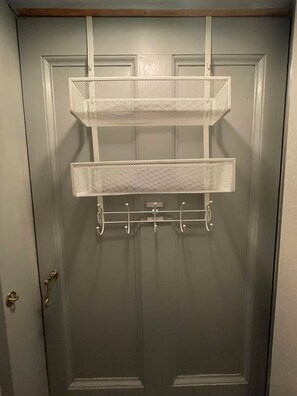 Une porte munie d’une étagère métallique et de crochets pour suspendre des objets.