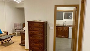 Una habitación con un aparador de madera, una silla, una mesa de comedor y una cocina visible a través de una puerta abierta.