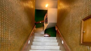 Una escalera con paredes de textura a ambos lados, barandilla y una lámpara en la parte superior.