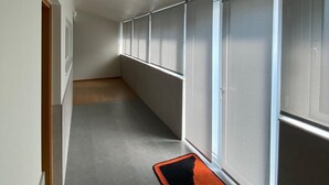 Un pasillo con piso de baldosas, un tapete negro y naranja, y ventanas amplias con persianas.
