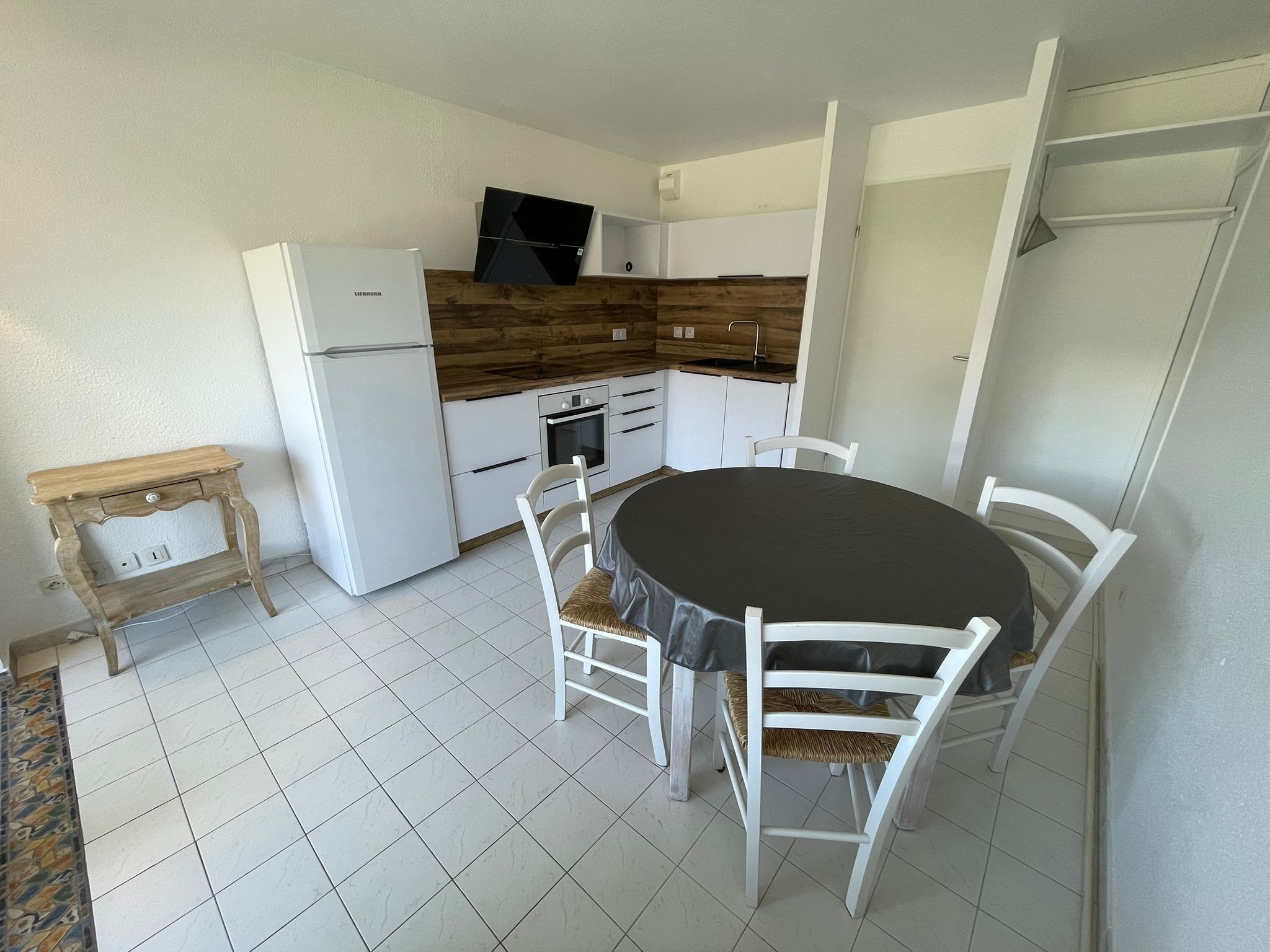 A compact kitchen with white cabinetry, a black countertop, and a round table with white chairs.