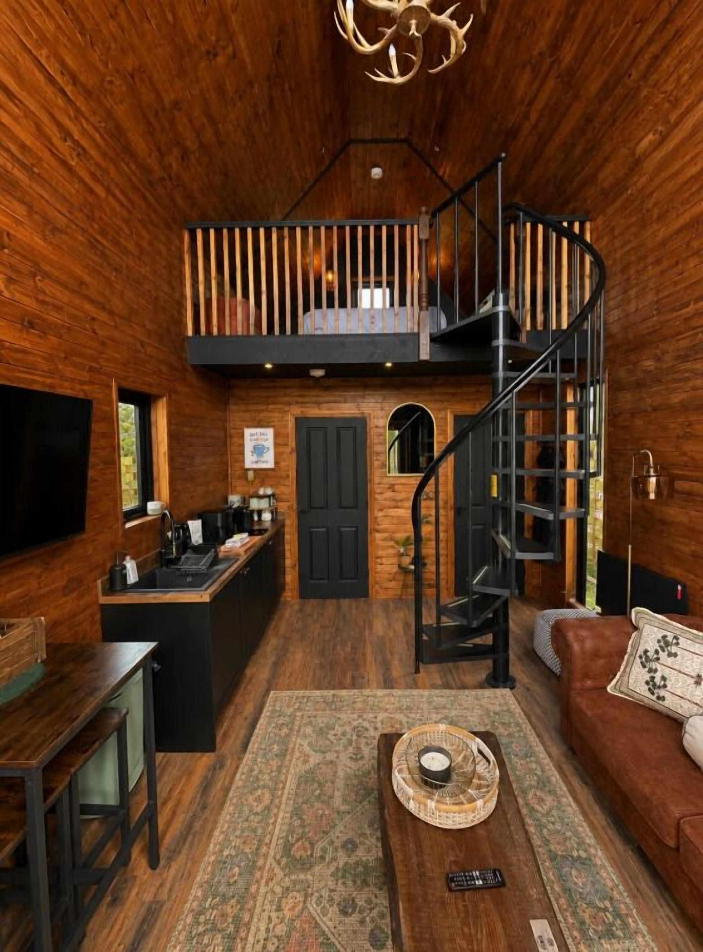 A wooden interior with a kitchen, dining area, and a staircase leading to a loft.