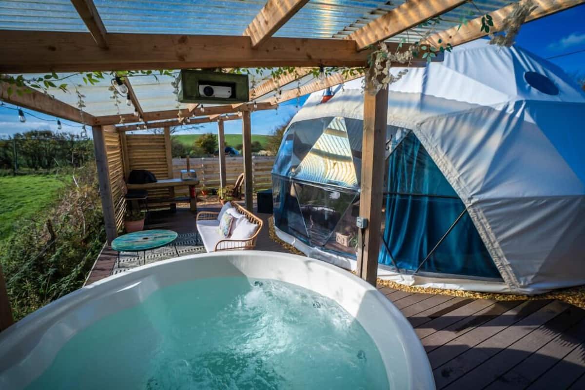 Un jacuzzi, una tienda de campaña y una terraza de madera con pérgola.
