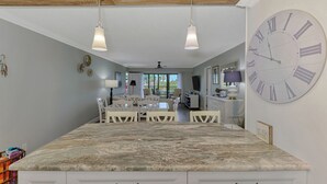 A spacious kitchen with a large marble countertop, two pendant lights, and a large wall clock. - Harbor Towers 418 - Tropical Sands Accommodations (Siesta Key)