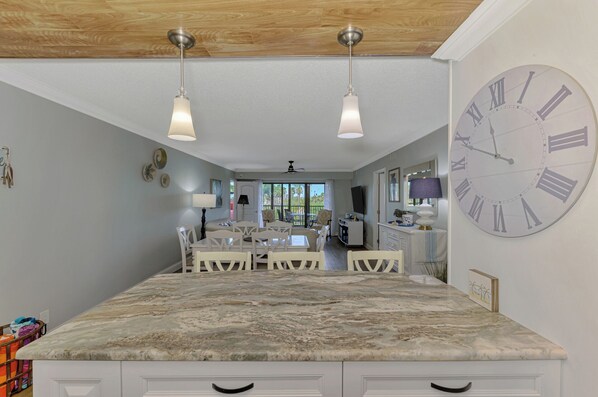 A spacious kitchen with a large marble countertop, two pendant lights, and a large wall clock. - Harbor Towers 418 - Tropical Sands Accommodations (Siesta Key)