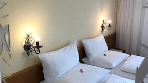 A hotel room with two beds, a nightstand, a wall-mounted lamp, and a window with curtains. - Gasthof Sprenger (Sillian)