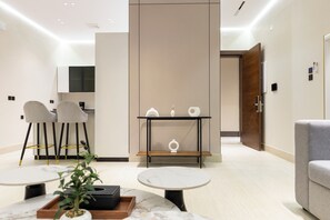 Una habitación de hotel moderna con zona de comedor, un sofá, una mesita y una planta en maceta.