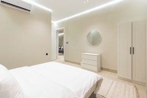 Ein Schlafzimmer mit Bett, Kommode, Kleiderschrank, Spiegel und Klimaanlage.