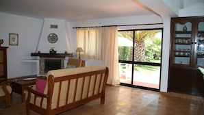 A living room with a sofa, a fireplace, a dining table with chairs, and a sliding glass door leading to a garden. - Country House 'Quinta Da Eira' with Private Pool, Wi-Fi and Air Conditioning (Lagoa)