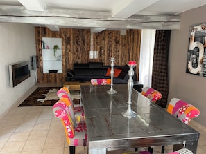 Ein Essbereich mit Holztisch, bunten Stühlen, einer schwarzen Couch und einem Kamin.