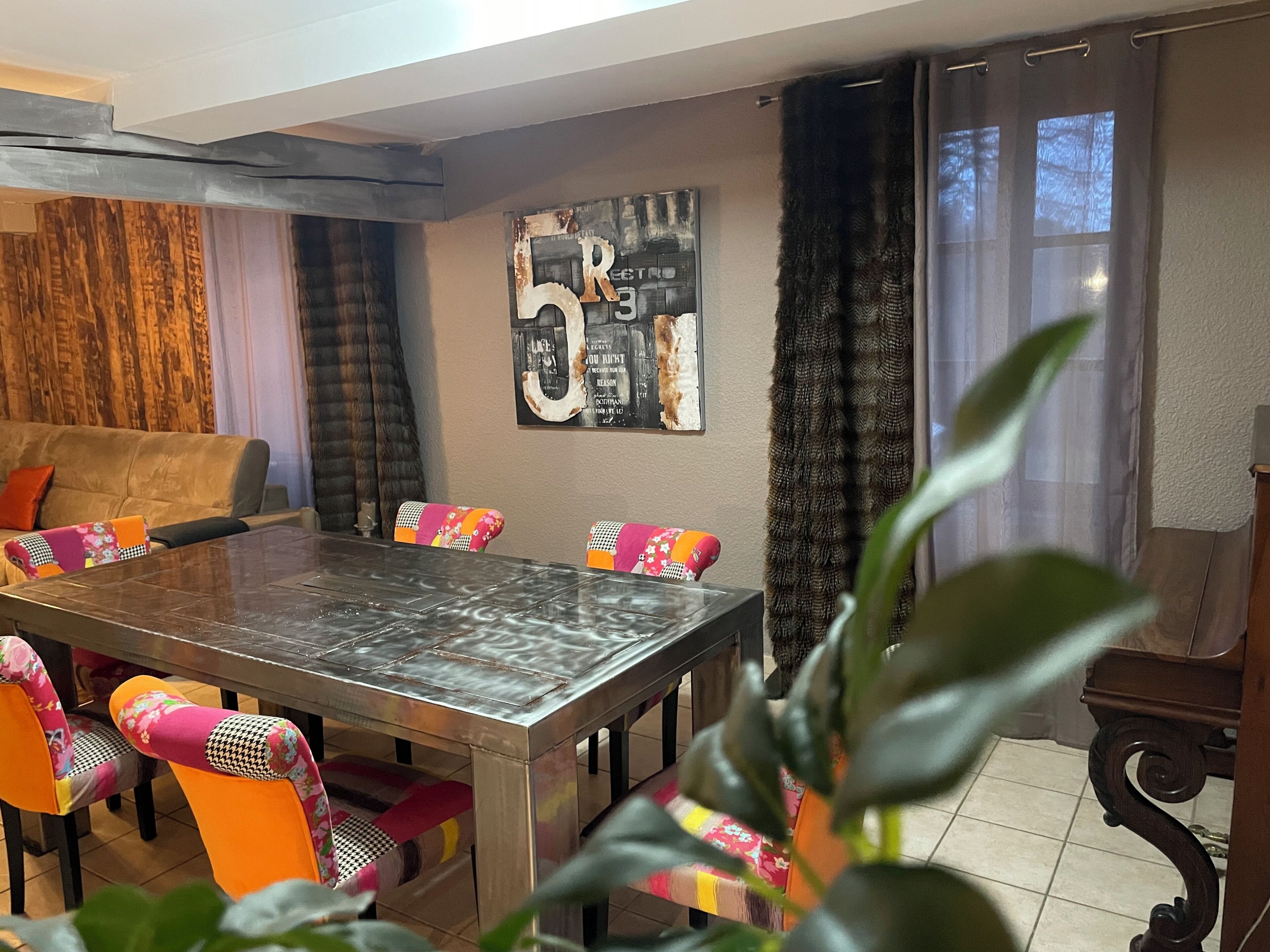 A dining area with a large table, colorful chairs, and a wall art piece.
