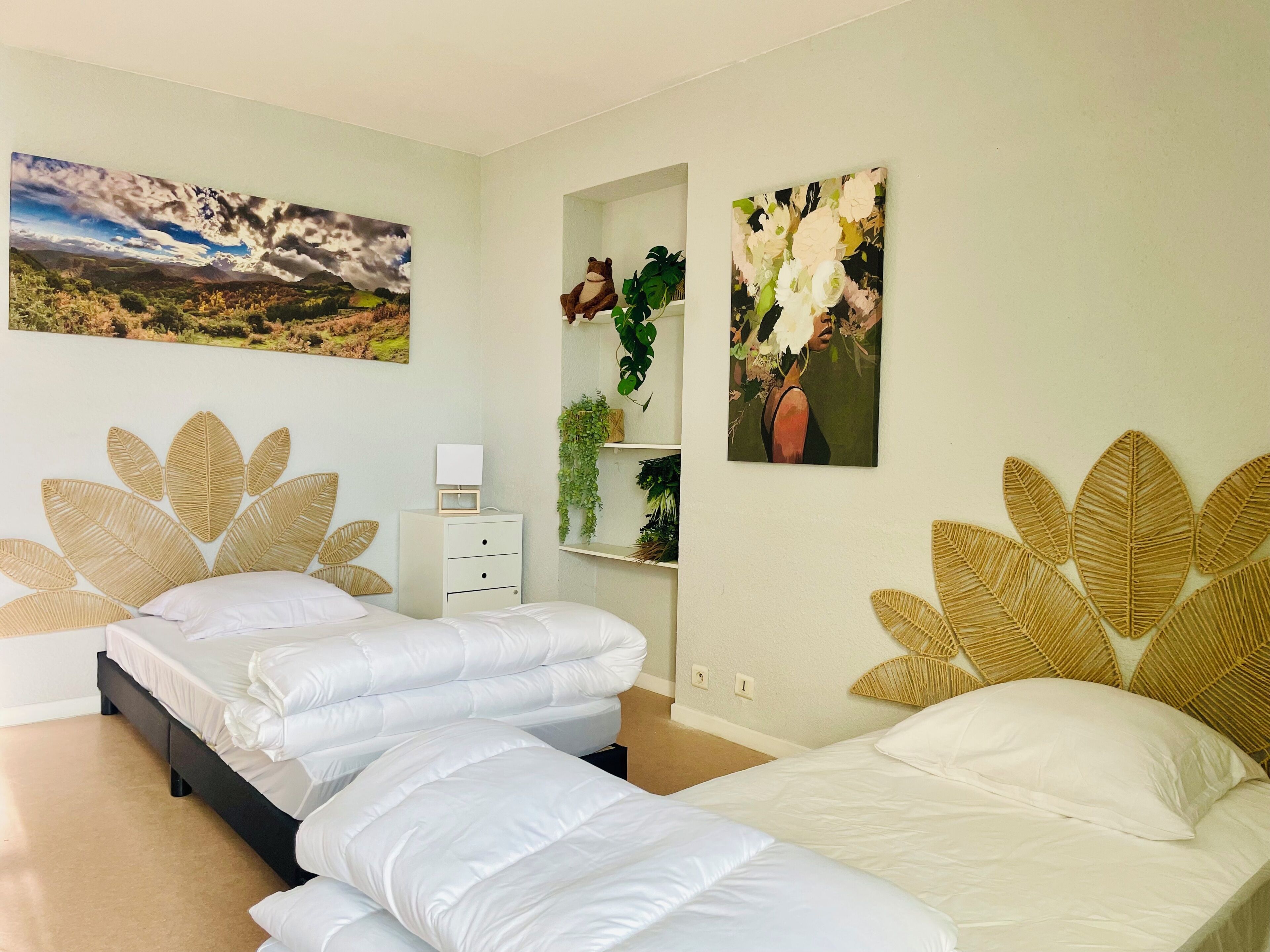 A bedroom with two beds, a nightstand, a small table, and wall art.