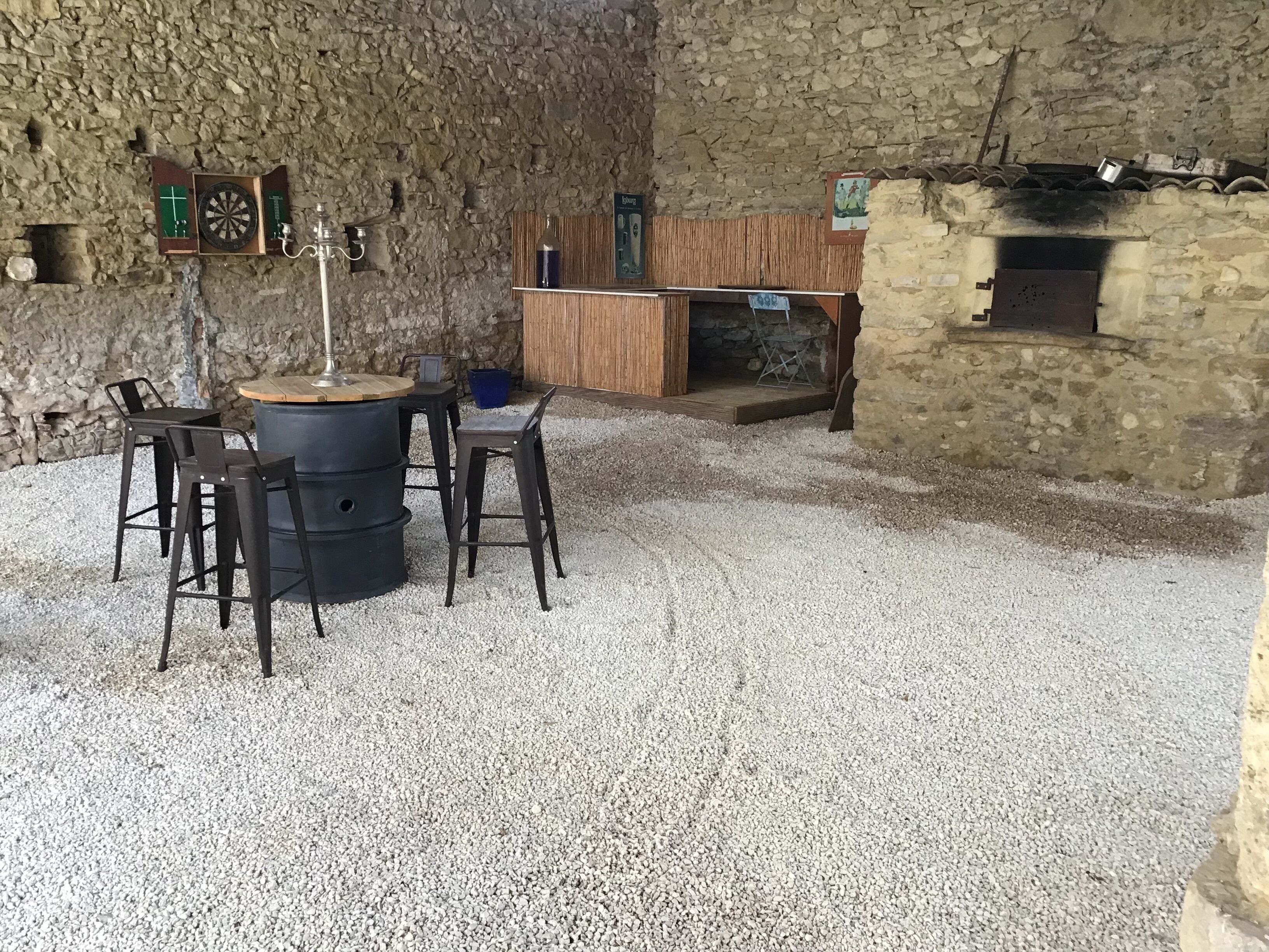 A rustic interior with a stone wall, a wooden bar, and a seating area with stools and a table.