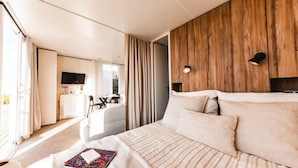 Ett modernt hotellrum med en stor säng, en vägg med träpanel som accent, en TV och en matplats som syns genom en öppen dörr.