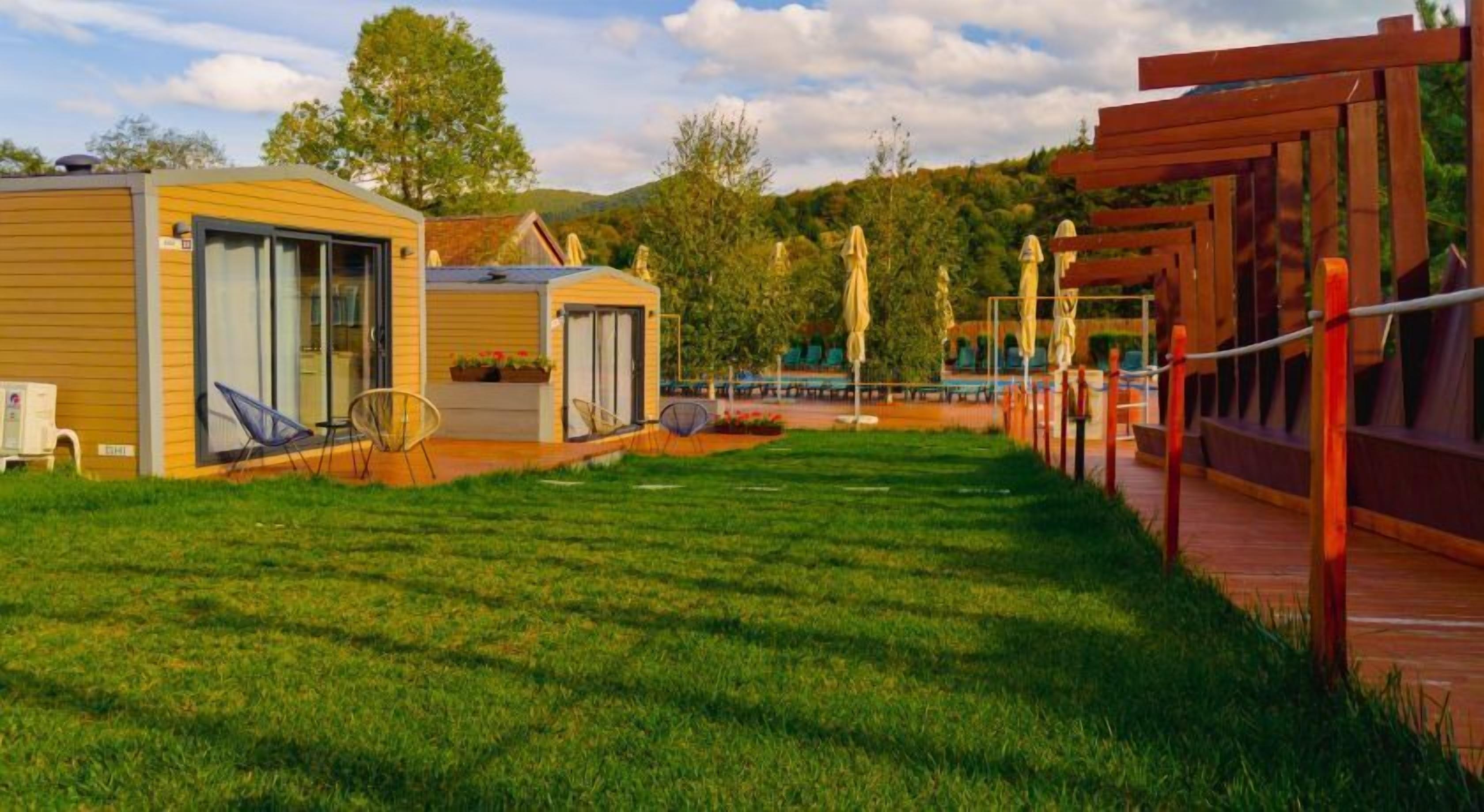 Un terrain de camping comprenant deux cabanes en bois, une zone herbeuse et une terrasse en bois.