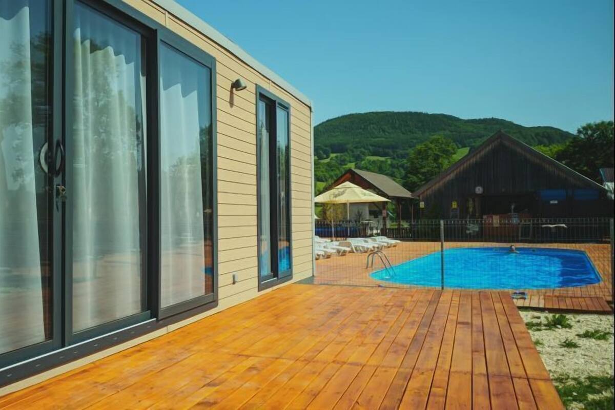 Ein modernes Haus mit einer Holzterrasse, einem Schwimmbad und Blick auf die Berge.