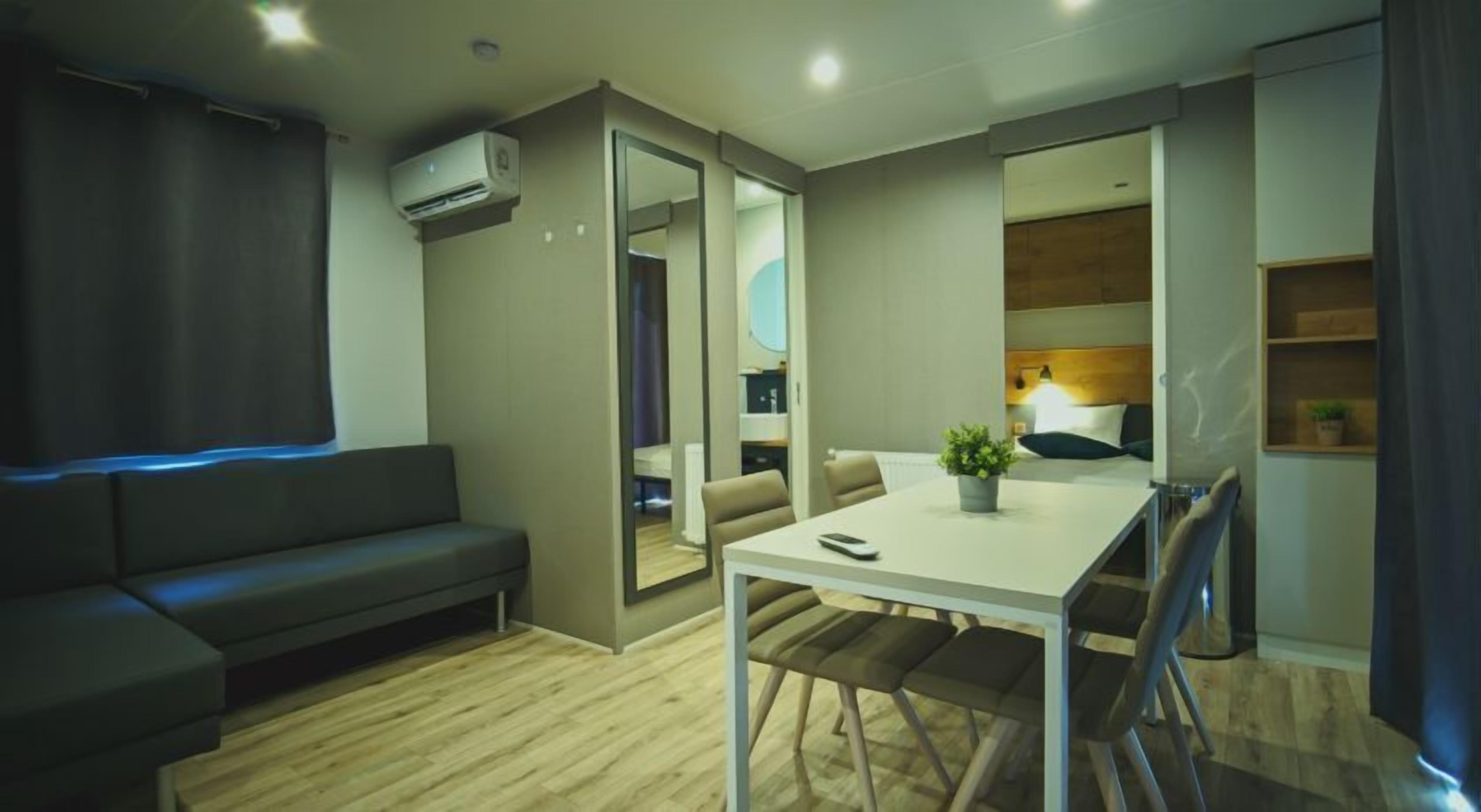 Et moderne hotelværelse med sofa, spisebord, en lille potteplante og en aircondition.