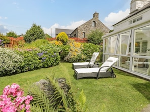 A garden with a stone building, a conservatory, and two lounge chairs. - Happy Landing (Harlech)
