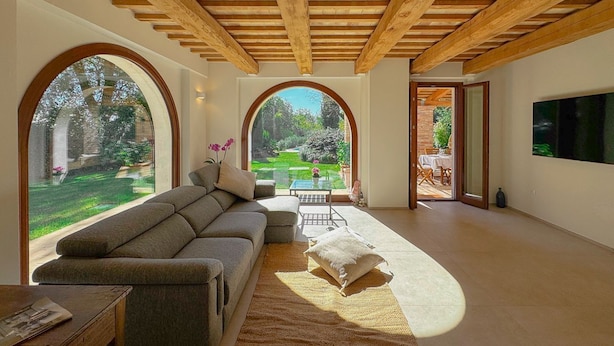 A modern living room with a sofa, a coffee table, and a TV. There are large windows and a view of a garden. - Villa in the Sibillini Mountains, Pool & Privacy (Sant'Angelo in Pontano)