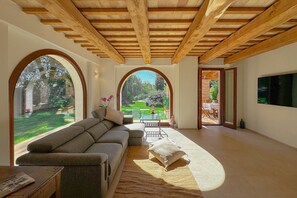 Un salon moderne avec un canapé, une table basse et un téléviseur. De grandes fenêtres offrent une vue sur un jardin.