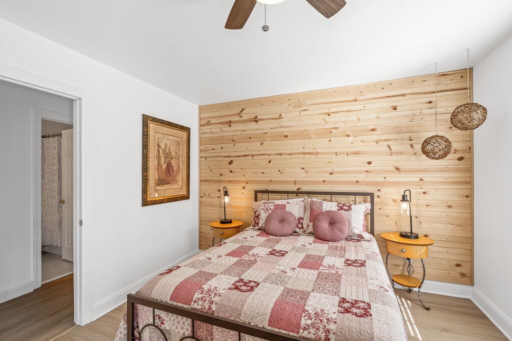 A bedroom with a wooden headboard, a quilted bedspread, two bedside tables with lamps, and a framed picture on the wall.