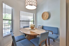 A dining area with a round wooden table, blue upholstered chairs, a woven wall hanging, and a hanging light fixture. - Updated Lakeview Retreat | Pools, Pickleball, Clubhouse & More | Near AMI & IMG (Bradenton)