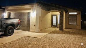 Eine Garage mit einem Pickup-Truck im Inneren, einer Tür zum Haus und einer gut beleuchteten Außenfassade.