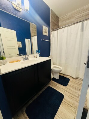 Een badkamer met een blauwe wand, een wit toilet, een witte wastafel, een zwart kastje en een douchegordijn.