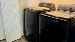 Ein Waschraum mit zwei schwarzen Waschmaschinen und Trocknern, einer weißen Tür und einem schwarzen Schrank über den Trocknern.
