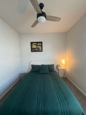 Een slaapkamer met een bed, een plafondventilator, een aan de muur hangend schilderij en een bedlampje.