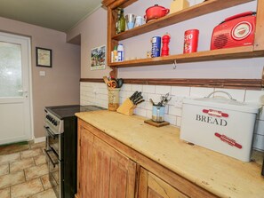 Uma cozinha com fogão a gás, armários de madeira, um saleiro e diversos utensílios de cozinha na bancada.