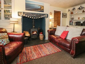 A cozy living room with leather sofas, a fireplace, a bookshelf, and a colorful rug. - Bodorwel Cottage (Penrhyndeudraeth)