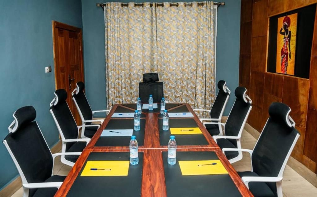 Un salón de conferencias con una larga mesa, sillas blancas y negras, y botellas de agua.