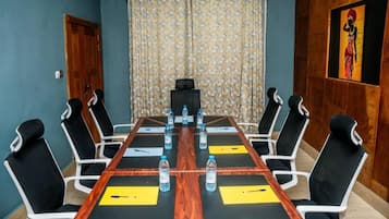 Un salón de conferencias con una larga mesa, sillas blancas y negras, y botellas de agua.