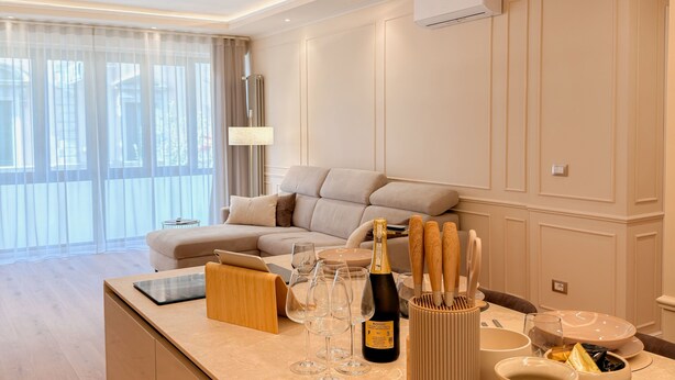 A modern kitchen with a central island, a dining area with a sofa, and a large window with sheer curtains. - The Golden Key
Your Charme Appartment in Tuscany (Arezzo)
