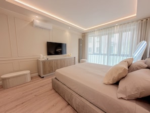 Une chambre moderne avec un grand lit, un téléviseur à écran plat, une table de chevet et une fenêtre ornée de rideaux légers.