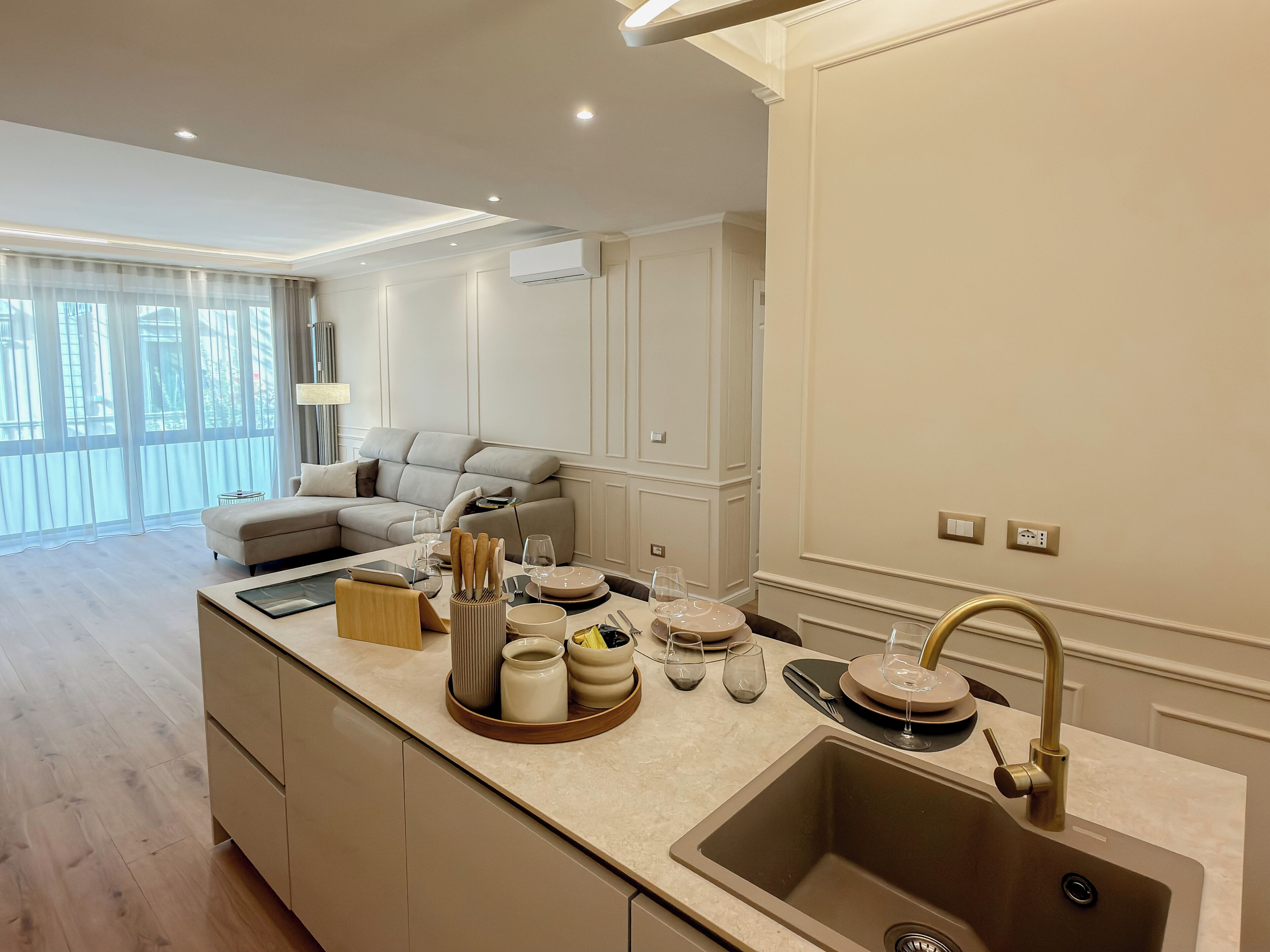 A modern kitchen with a built-in island, a sink with a gold faucet, and a dining area with a sofa and dining table.
