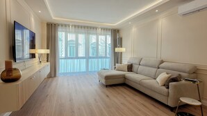 A modern living room with a sectional sofa, a flat-screen TV, and a large window with sheer curtains. - The Golden Key
Your Charme Appartment in Tuscany (Arezzo)