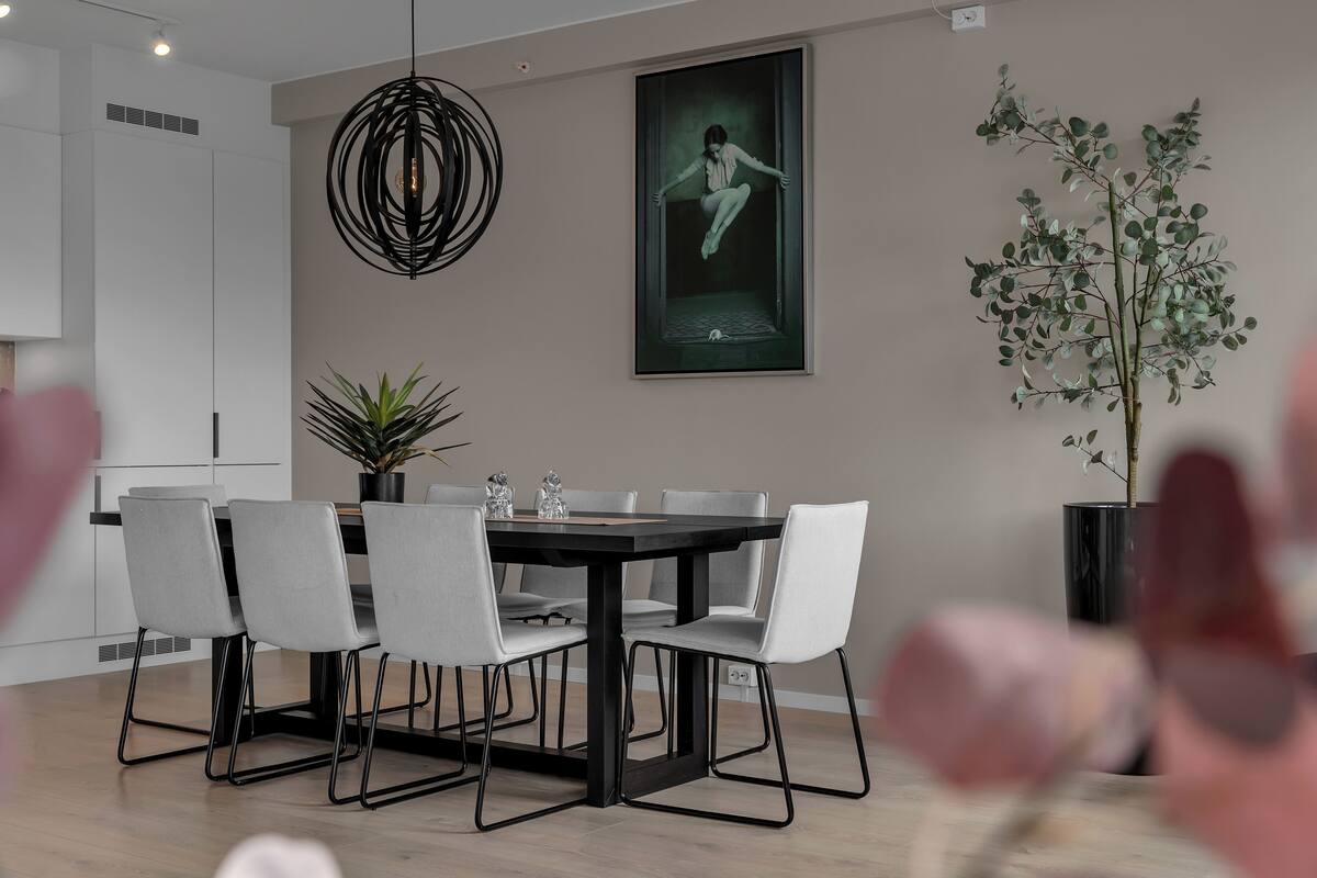 A modern dining area with a black table, white chairs, a pendant light, a framed artwork, and a potted plant.