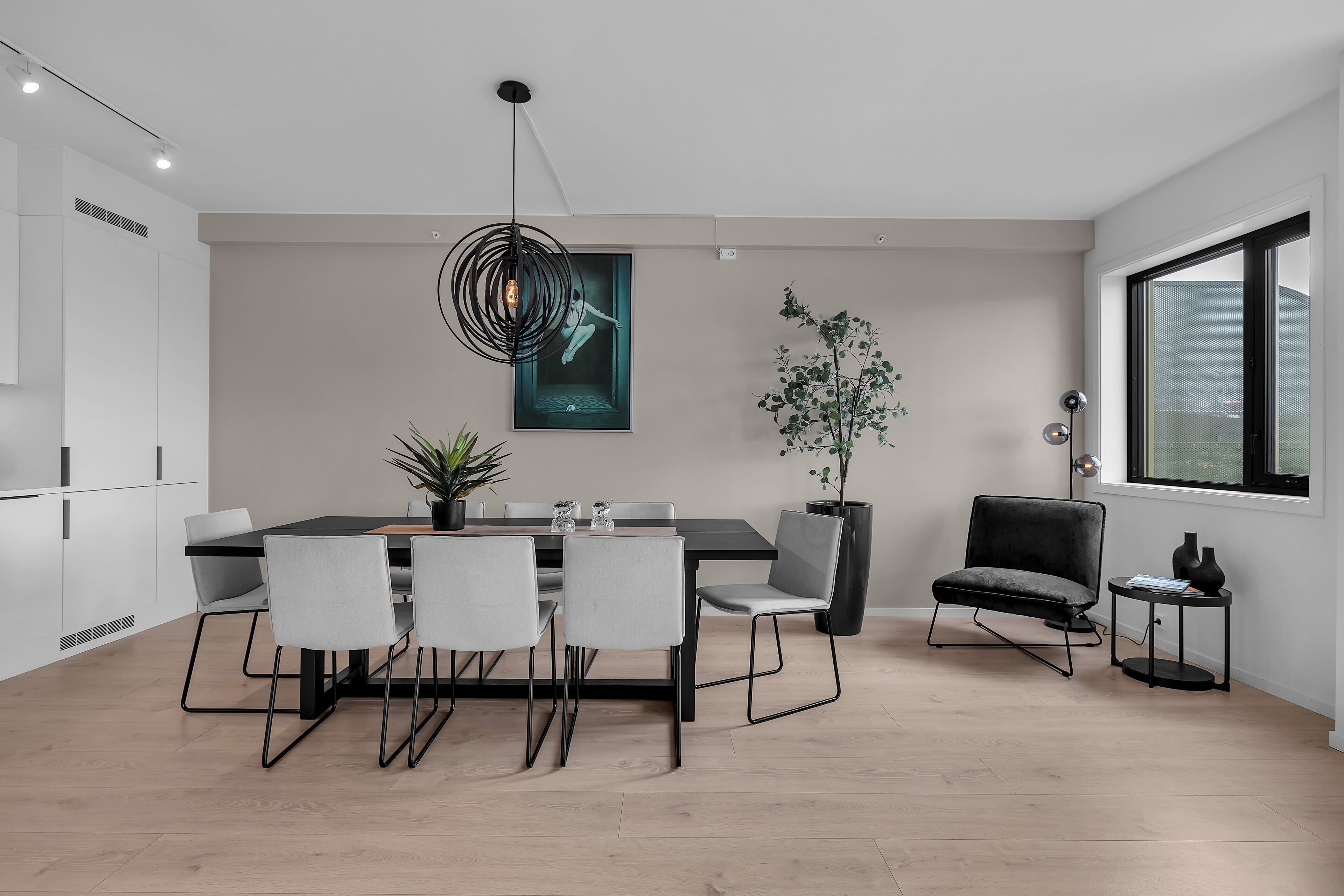 A modern dining area with a black table, white chairs, a hanging light fixture, and a potted plant.