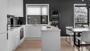 A modern kitchen with white cabinets, a central island, and a dining area with a table and chairs. - TotalApartments Gjøa Premium (Tromsø)