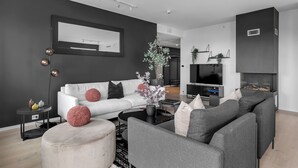 A modern living room with a white sofa, grey armchairs, a black coffee table, and a large flat-screen TV. - TotalApartments Gjøa Premium (Tromsø)