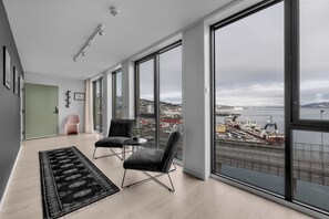 A spacious room with large windows, a black rug, two chairs, and a view of a harbor.