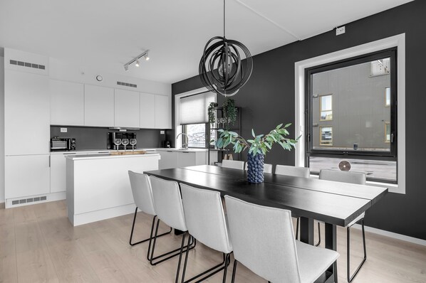 A modern kitchen with white cabinets, a central island, and a dining area with a dark table and chairs.