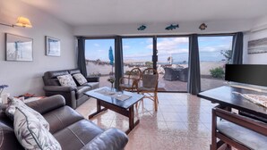 A living room with a sofa, coffee table, and chairs, a television, and a view of the outdoors. - Casa Buenavista • Pool • Ocean views • Beach 2 min • LVH (Famara)