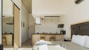 A modern hotel room with a bed, bedside table, and a view of the kitchen area. - Portal Arevalo in Palermo by Magno | 81 (Buenos Aires)