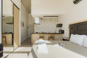 A modern hotel room with a bed, bedside table, and a view of the kitchen area. - Portal Arevalo in Palermo by Magno | 81 (Buenos Aires)